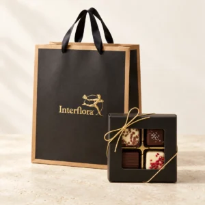 Svart presentpåse från Interflora med sidenhandtag och en svart chokladask med fyra praliner och guldsnöre.